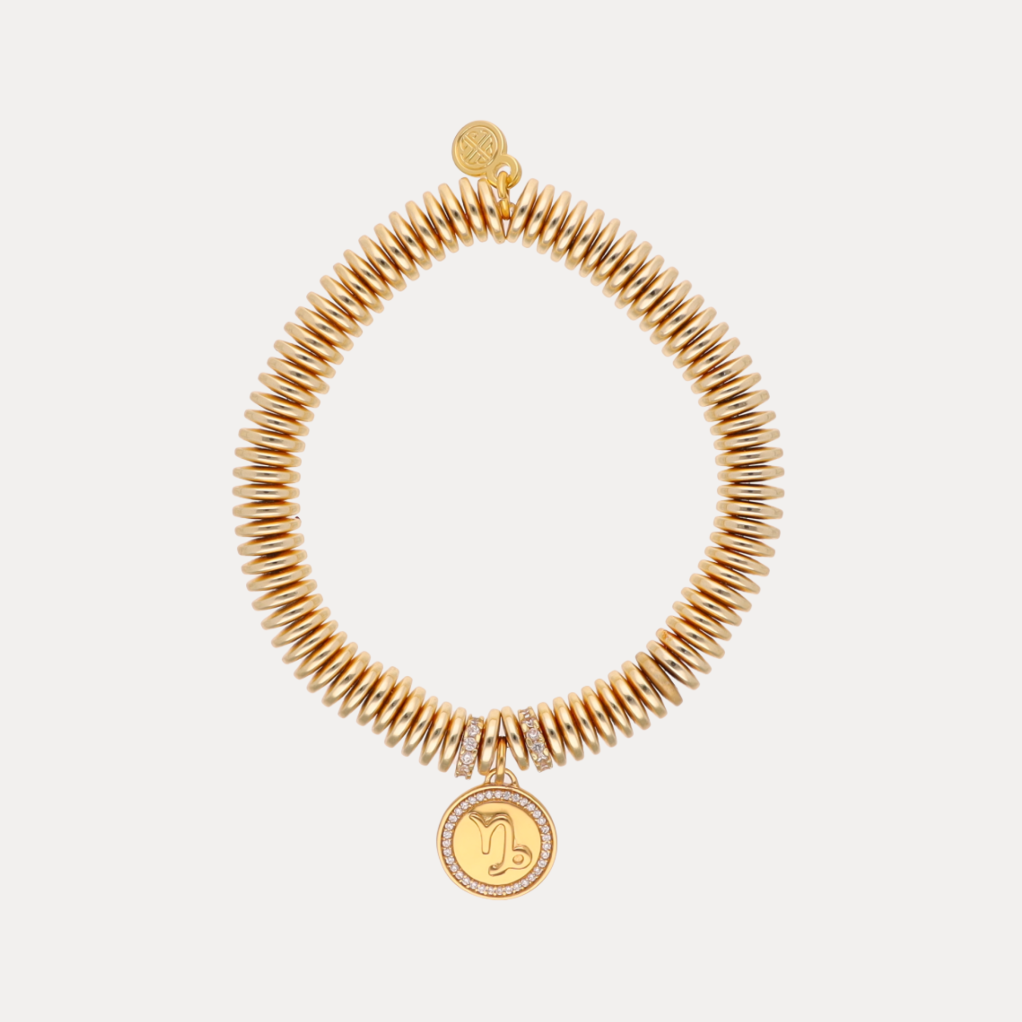 Gold coil bracelet with a circular charm on a light beige background