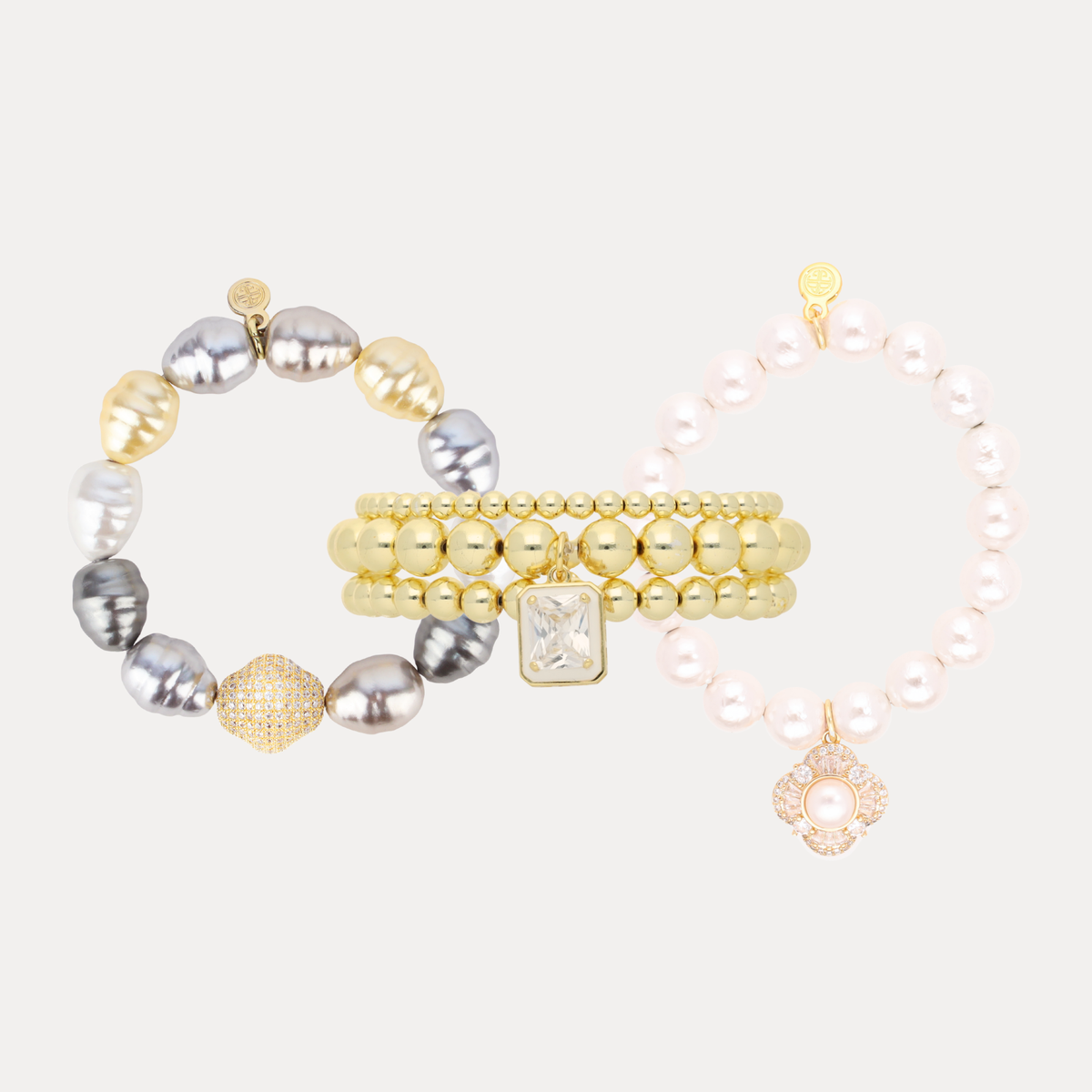 BuDhaGirl bracelet bundle featuring gray and white pearl bracelets with three gleaming gold bangles and delicate charm details for women on a neutral background