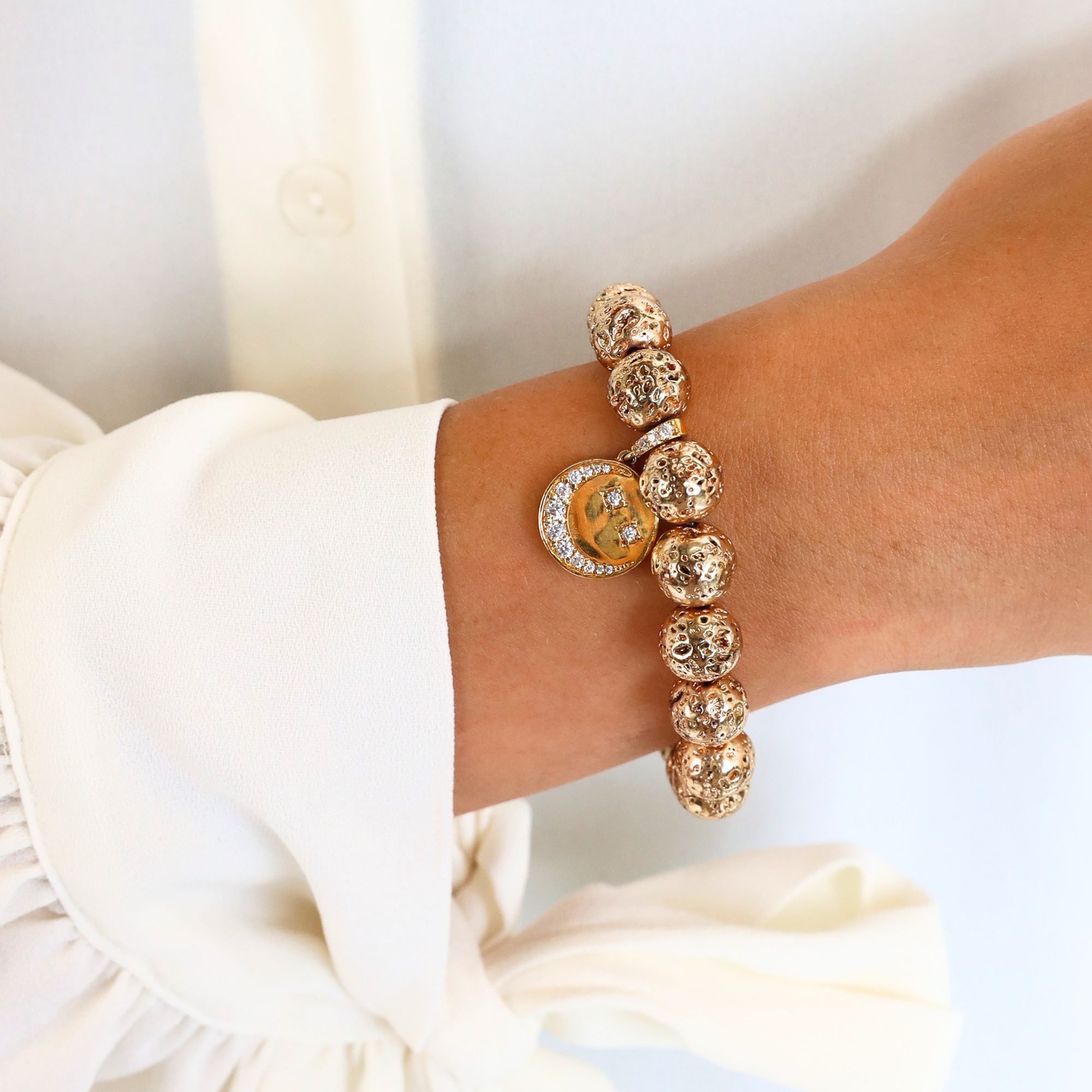Gold bracelet with a decorative clasp on a wrist against a neutral background