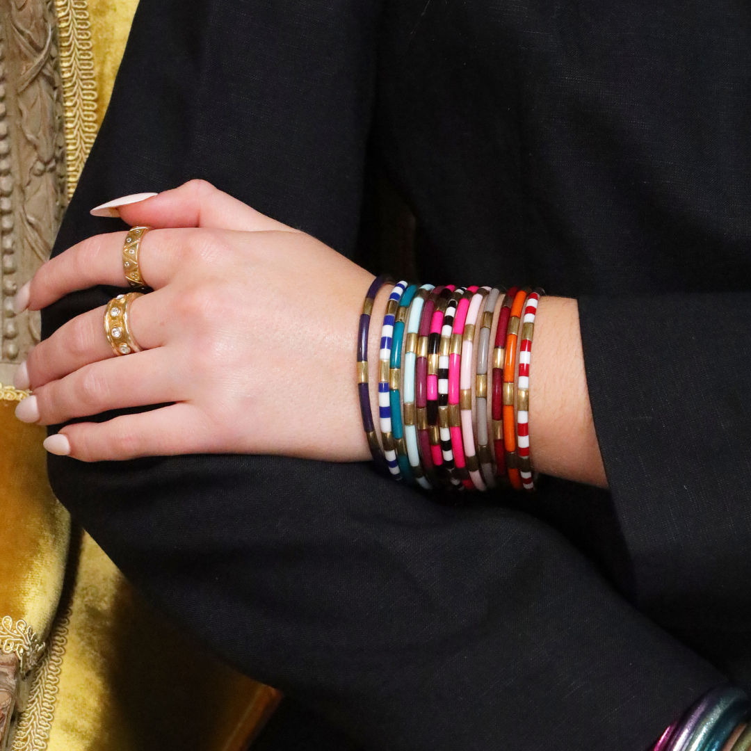 Hand wearing colorful bracelets with gold rings on a black sleeve.