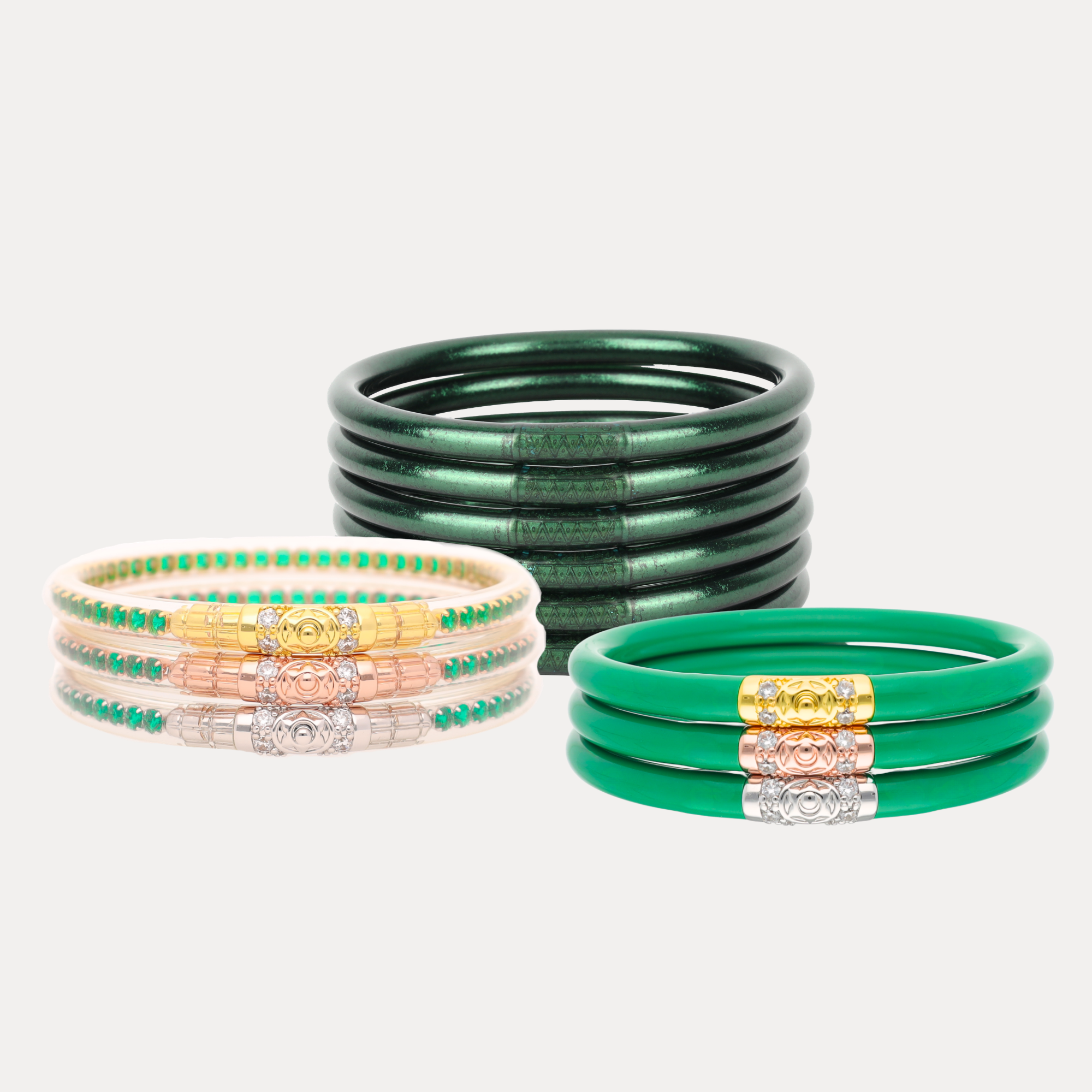 Four stacks of bangles on a light gray background: a stack of dark green bangles, a stack of green and turquoise beaded bangles with silver-toned connectors, a stack of green and gold beaded bangles with silver-toned connectors, and a stack of solid green bangles with gold and silver-toned connectors.