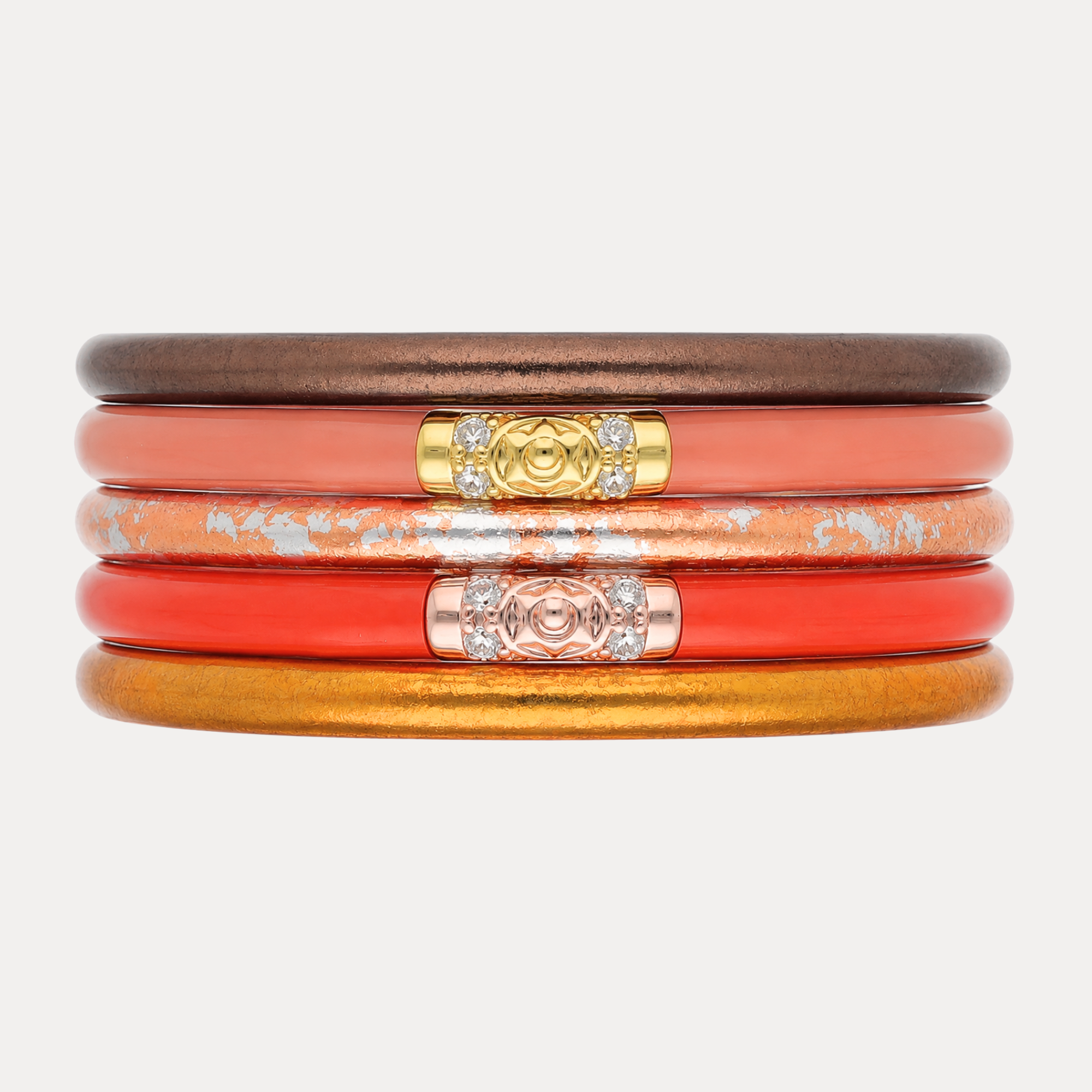 A stack of five slim bangles with a glossy finish in dark brown, coral, orange, and gold tones, accented with gold and rose gold clasp details set with small clear crystals, on a light gray background.