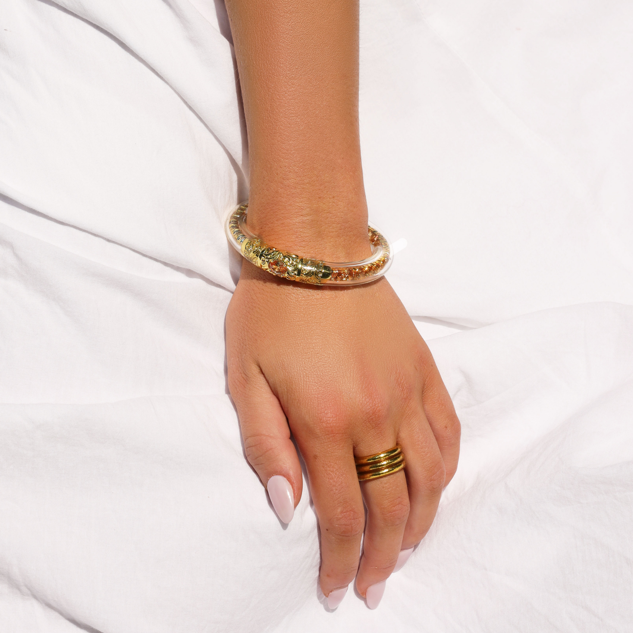 a hand with a gold bracelet on a white surface