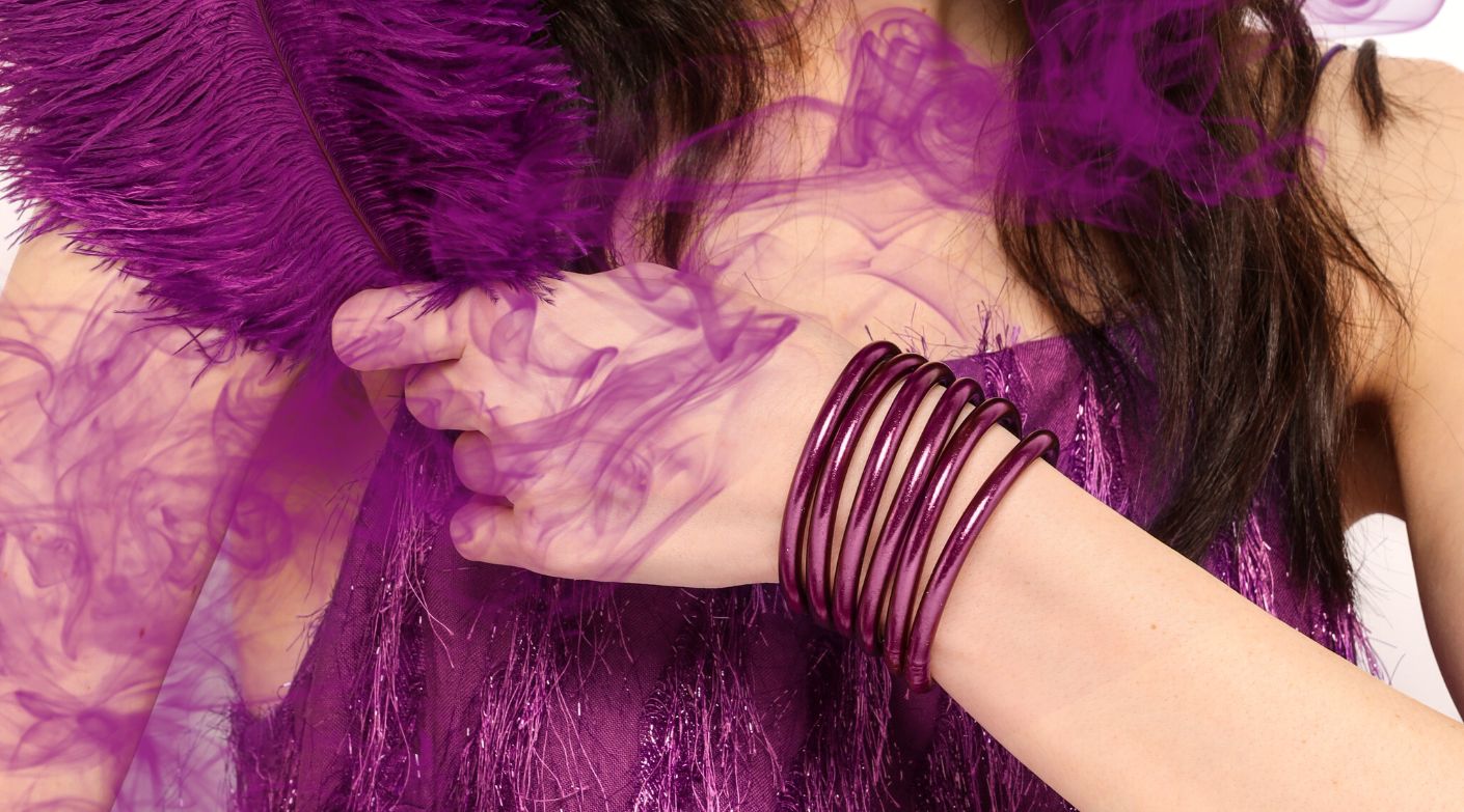 Woman in purple dress holding purple feather wearing BuDhaGirl Purple Amethyst All Weather Bangles | BuDhaBrief by BuDhaGirl 
