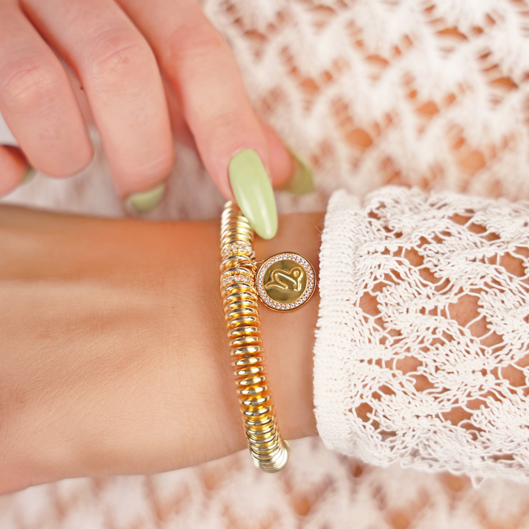 Gold bracelet with a logo on a wrist against a textured background