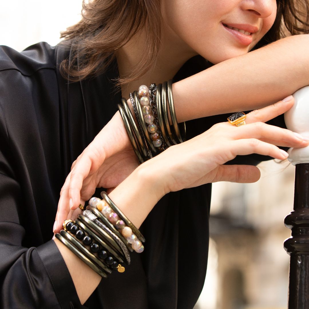 A photo of a woman's wrist adorned with gold, silver, flint all weather bangles, and bead bangles and bracelets.
