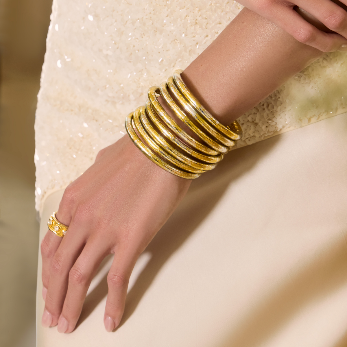BuDhaGirl gold bangle bracelets for women stacked on a wrist against a softly textured cream outfit