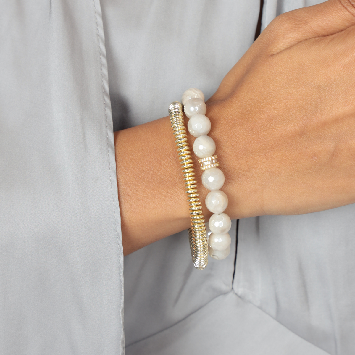 BuDhaGirl bangle bracelet set worn on a wrist with cloudy grey faceted beads and a textured gold tone bangle against a soft grey background