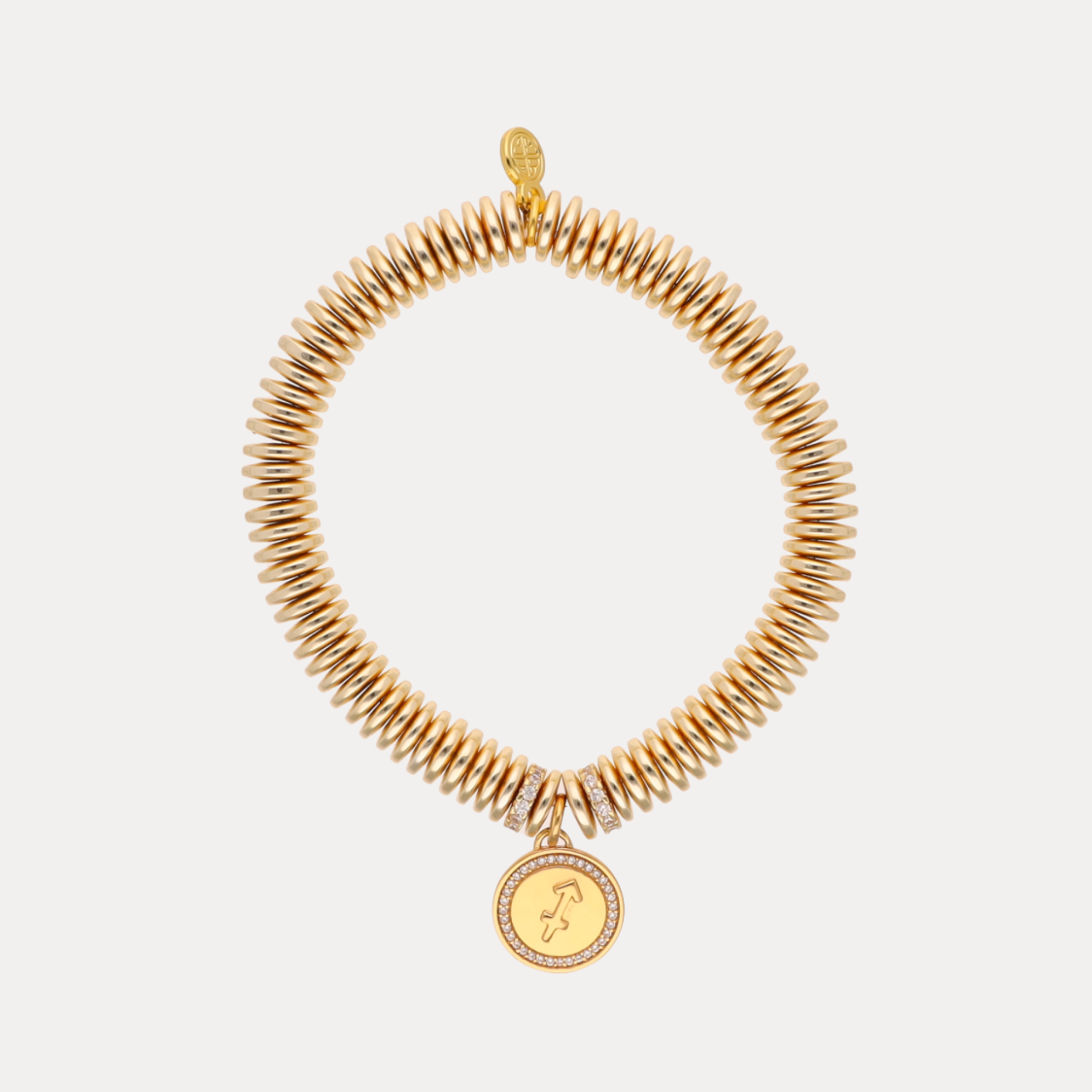 Gold coil bracelet with a circular charm on a light gray background