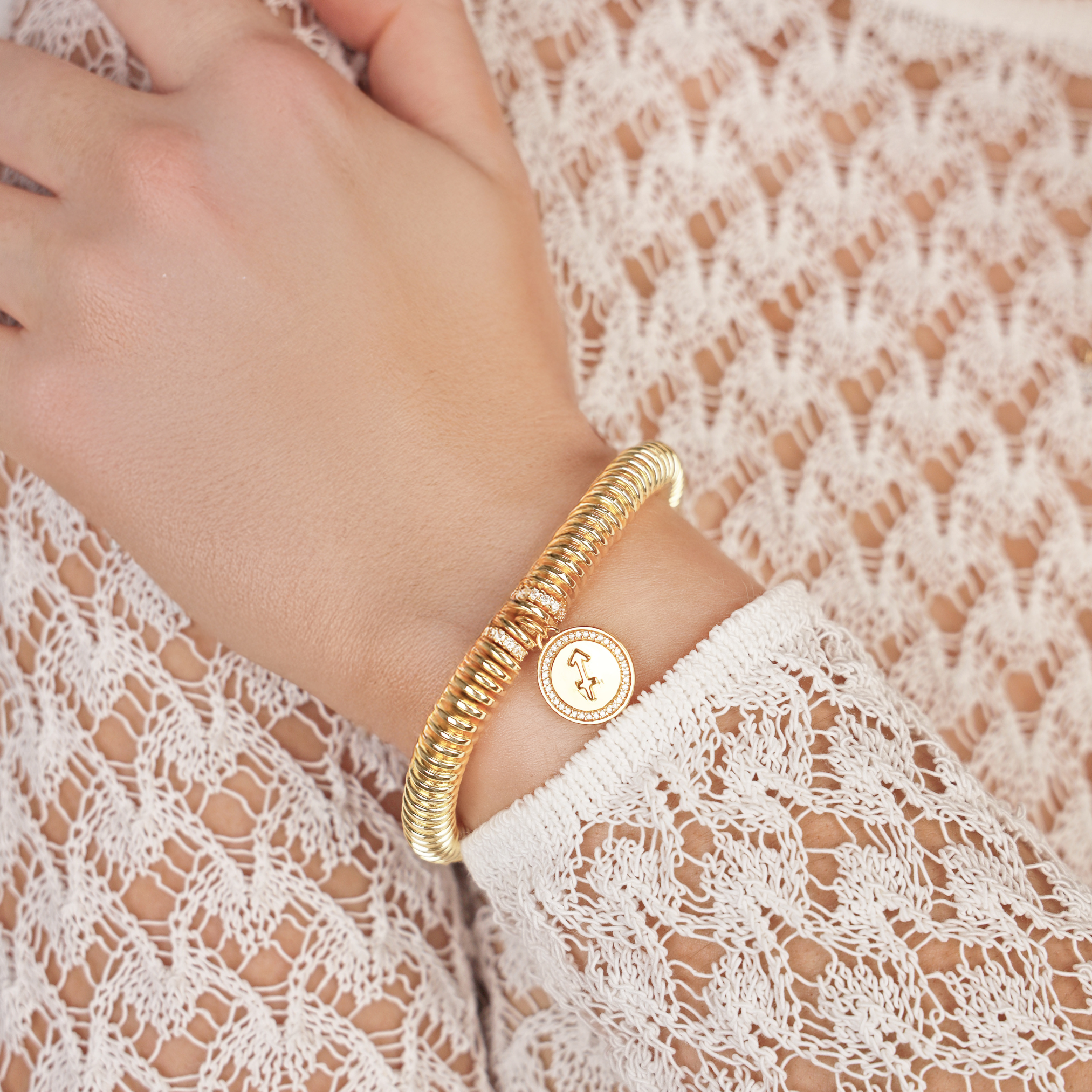 Gold bracelet on a wrist with a lace garment in the background