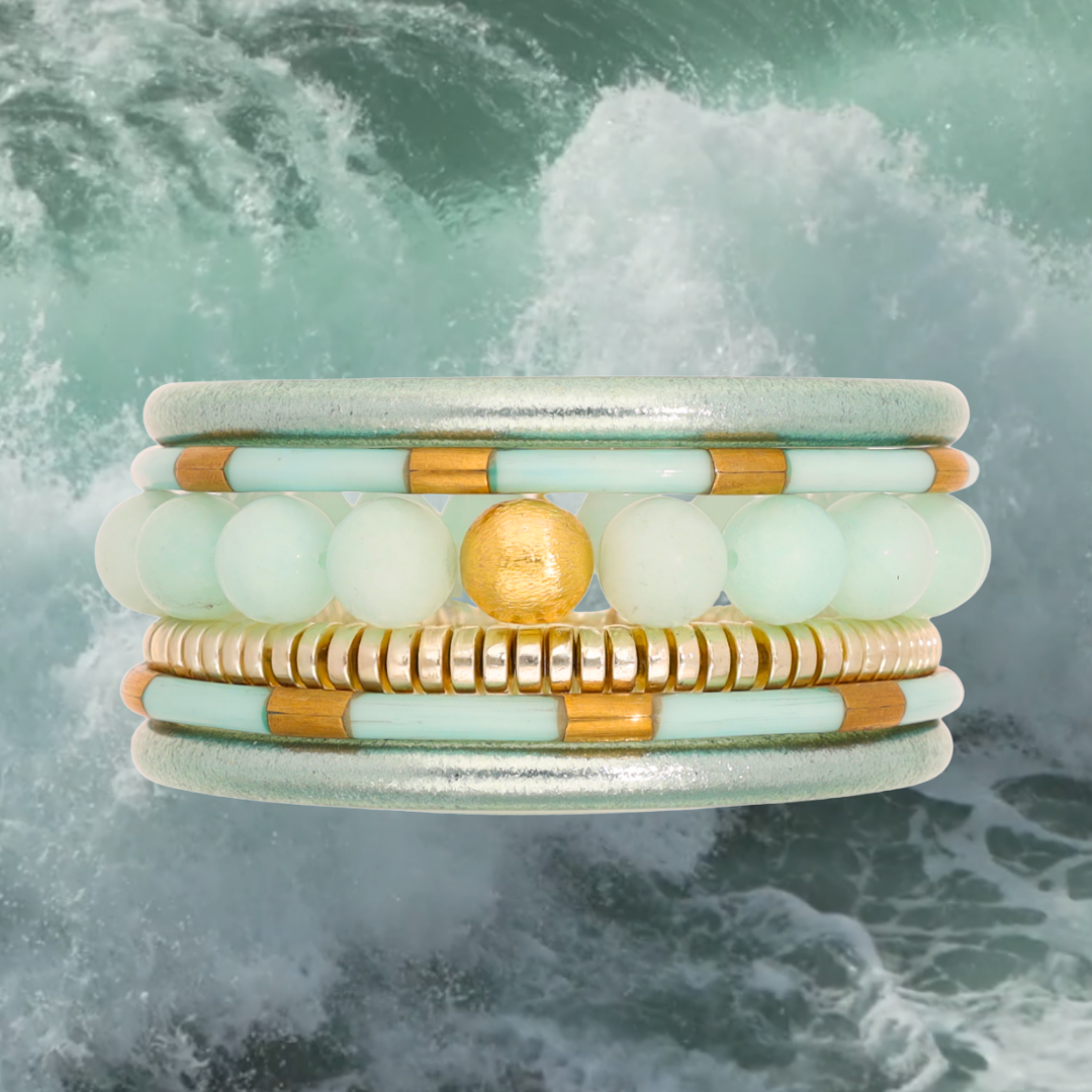 Stack of bracelets with gold and green beads against a water background