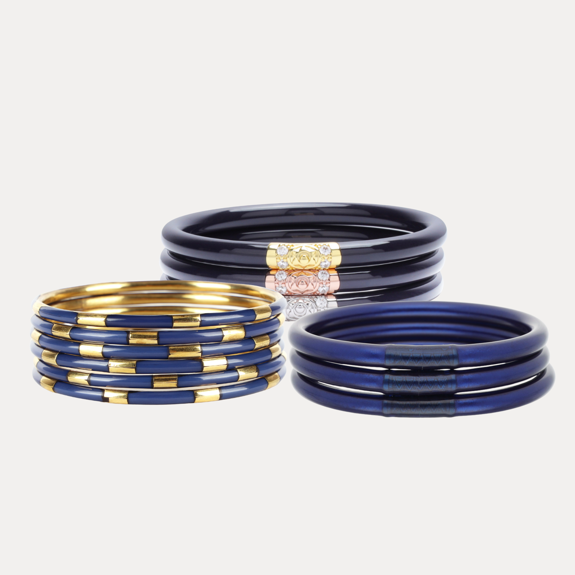Three sets of bangles on a light gray background: one set of dark navy blue bangles with a gold-toned accent, one set of navy blue bangles with gold-toned spacer bands, and one set of navy blue bangles with a rhinestone-embellished gold-toned accent.