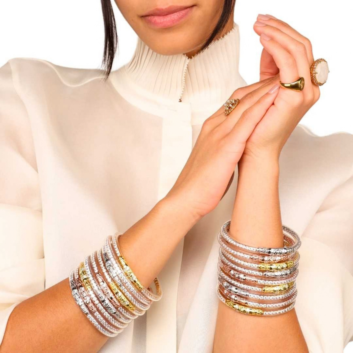 BuDhaGirl clear crystal and yellow gold bangle bracelets for women stacked on both wrists with coordinating rings and an elegant white blouse