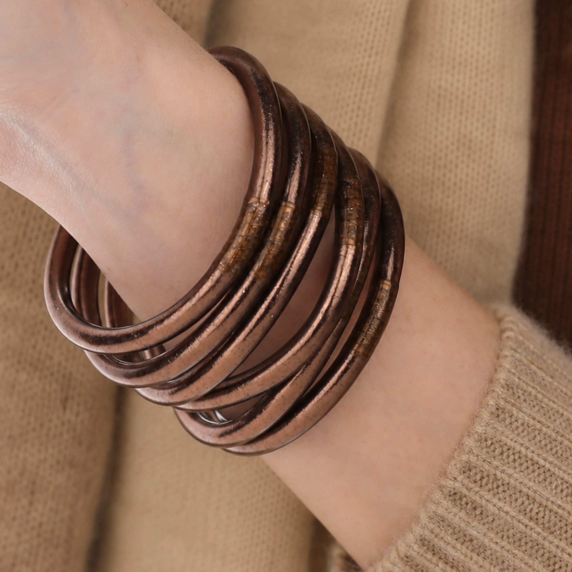 A close-up of a person's wrist wearing a stack of meteorite all weather bangles over a beige knit sweater.