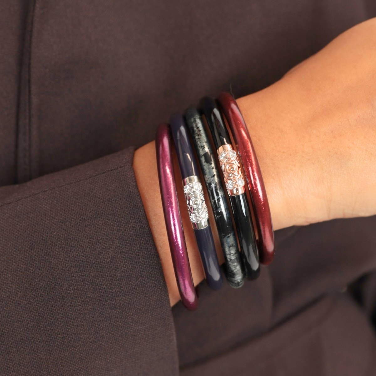 Stack of glossy burgundy navy and black bangle bracelets with ornate silver accents worn on a wrist against dark clothing for women